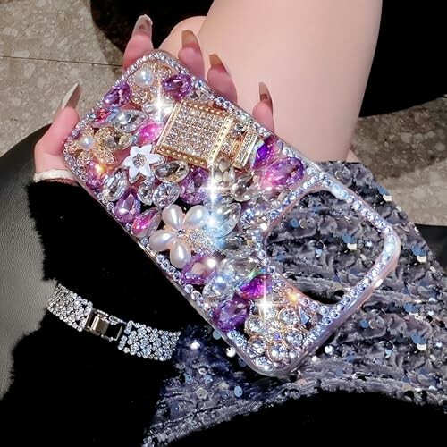 Hand holding a decorated rhinestone phone case with jewels and flowers.